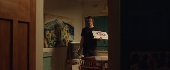 Movie still from “Little Monsters” (2019), directed by Abe Forsythe – A man standing in a room holding a box of pizza; Medium shot, Low angle