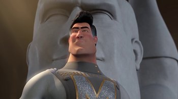 Movie still from “Megamind” (2010), directed by Tom McGrath – A man in a gray suit standing in front of a statue; Close Up shot, Low angle