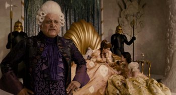 Movie still from “Mirror Mirror” (2012), directed by Tarsem Singh – A man in a wig and wig stands in front of a bed; Medium shot, Over the shoulder angle