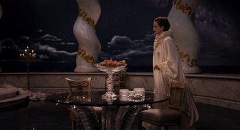 Movie still from “Mirror Mirror” (2012), directed by Tarsem Singh – A woman standing in front of a table with a bowl of fruit; Wide shot, High angle