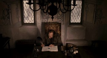 Movie still from “Mirror Mirror” (2012), directed by Tarsem Singh – A man sitting at a table writing on a piece of paper; Medium shot, High angle