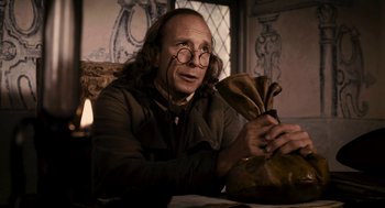 Movie still from “Mirror Mirror” (2012), directed by Tarsem Singh – A man sitting at a table holding a bag; Medium shot, Low angle