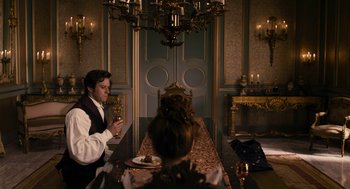 Movie still from “Mirror Mirror” (2012), directed by Tarsem Singh – A man and a woman sitting at a dinner table in front of a chandelier; Wide shot, High angle