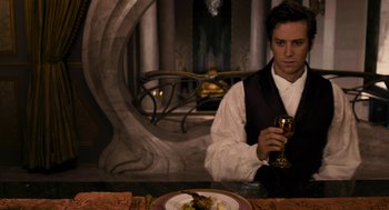 Movie still from “Mirror Mirror” (2012), directed by Tarsem Singh – A man sitting in front of a plate of food holding a wine glass; Medium shot, Over the shoulder angle