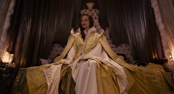 Movie still from “Mirror Mirror” (2012), directed by Tarsem Singh – A woman sitting on top of a couch wearing a dress; Medium shot, Low angle