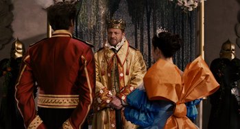 Movie still from “Mirror Mirror” (2012), directed by Tarsem Singh – A man wearing a crown standing next to two other people; Medium shot, Over the shoulder angle