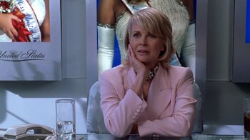 Movie still from “Miss Congeniality” (2000), directed by Donald Petrie – A woman sitting at a table in front of a poster; Close Up shot, Over the shoulder angle