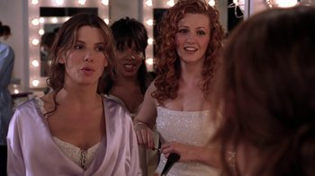 Movie still from “Miss Congeniality” (2000), directed by Donald Petrie – A group of women standing next to each other in front of lights; Medium shot, Over the shoulder angle
