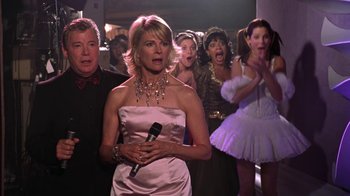 Movie still from “Miss Congeniality” (2000), directed by Donald Petrie – A group of people standing in front of a woman holding a microphone; Medium shot, Over the shoulder angle