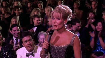 Movie still from “Miss Congeniality” (2000), directed by Donald Petrie – A woman is holding a microphone in front of a crowd of people; Medium shot, Over the shoulder angle