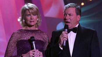 Movie still from “Miss Congeniality” (2000), directed by Donald Petrie – A man and a woman holding microphones on a stage; Medium shot, Low angle