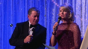 Movie still from “Miss Congeniality” (2000), directed by Donald Petrie – A man and a woman holding microphones in front of a curtain; Medium shot, High angle