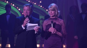 Movie still from “Miss Congeniality” (2000), directed by Donald Petrie – A man and a woman standing next to each other holding microphones; Medium shot, Over the shoulder angle