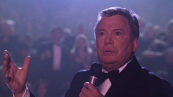 Movie still from “Miss Congeniality” (2000), directed by Donald Petrie – An older man in a tuxedo holding a microphone in front of an audience; Close Up shot, Low angle