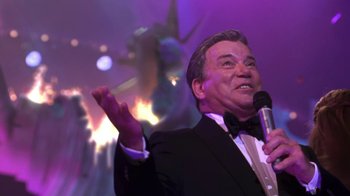 Movie still from “Miss Congeniality” (2000), directed by Donald Petrie – A man in a tuxedo holding a microphone and smiling; Medium shot, Low angle
