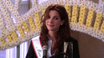 Movie still from “Miss Congeniality” (2000), directed by Donald Petrie – A woman with long brown curly hair wearing a white sash; Medium shot, Over the shoulder angle