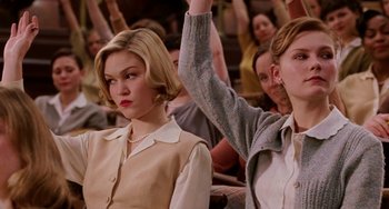 Movie still from “Mona Lisa Smile” (2003), directed by Mike Newell – Two women sitting in front of a group of people holding up their hands; Medium shot, Low angle