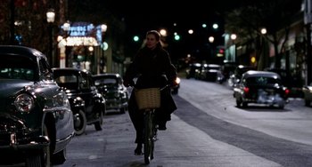 Movie still from “Mona Lisa Smile” (2003), directed by Mike Newell – A woman riding a bike down a street at night; Wide shot, High angle