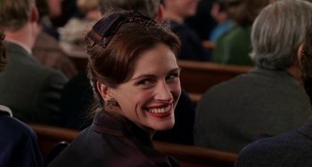 Movie still from “Mona Lisa Smile” (2003), directed by Mike Newell – A woman smiling while sitting in a crowd of people; Close Up shot, Over the shoulder angle