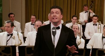 Movie still from “Mona Lisa Smile” (2003), directed by Mike Newell – A man in a tuxedo is singing in front of a group of men; Medium shot, Low angle