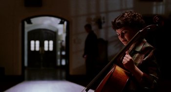 Movie still from “Mona Lisa Smile” (2003), directed by Mike Newell – A person playing a cello in a room; Medium shot, Over the shoulder angle