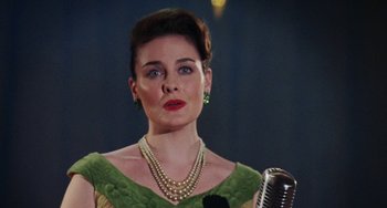 Movie still from “Mona Lisa Smile” (2003), directed by Mike Newell – A woman in a green dress holding a microphone in front of her face; Close Up shot, Low angle