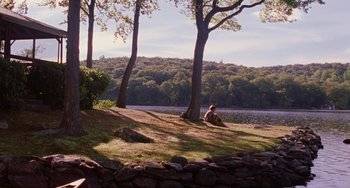 Movie still from “Mona Lisa Smile” (2003), directed by Mike Newell – A person sitting on the grass near a body of water; Extreme Wide shot, High angle