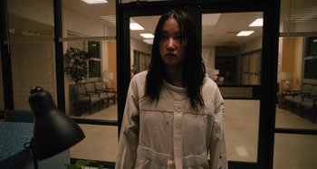 Movie still from “Mona Lisa and the Blood Moon” (2021), directed by Ana Lily Amirpour – A woman standing in front of a glass door in a room; Medium shot, Low angle