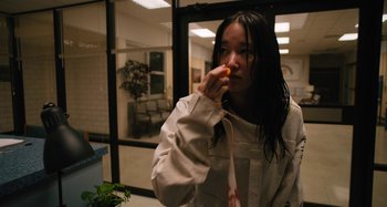 Movie still from “Mona Lisa and the Blood Moon” (2021), directed by Ana Lily Amirpour – A woman eating an orange while standing in front of a window; Medium shot, Over the shoulder angle