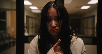 Movie still from “Mona Lisa and the Blood Moon” (2021), directed by Ana Lily Amirpour – A woman with long black hair is holding an orange object in her mouth; Close Up shot, High angle