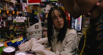 Movie still from “Mona Lisa and the Blood Moon” (2021), directed by Ana Lily Amirpour – A young woman sitting at a table in front of a counter; Close Up shot, Over the shoulder angle
