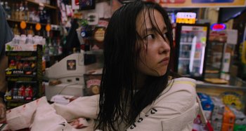 Movie still from “Mona Lisa and the Blood Moon” (2021), directed by Ana Lily Amirpour – A woman with long black hair sitting in front of a store; Close Up shot, Low angle