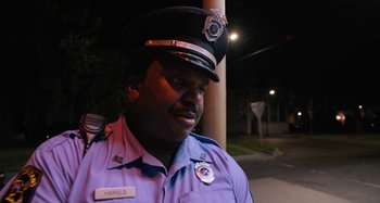 Movie still from “Mona Lisa and the Blood Moon” (2021), directed by Ana Lily Amirpour – A man in a police uniform standing next to a lamp post; Close Up shot, Over the shoulder angle