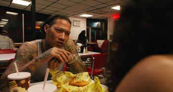 Movie still from “Mona Lisa and the Blood Moon” (2021), directed by Ana Lily Amirpour – A man sitting in front of a table with a sandwich; Close Up shot, Over the shoulder angle