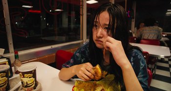 Movie still from “Mona Lisa and the Blood Moon” (2021), directed by Ana Lily Amirpour – A woman sitting at a table with a sandwich in front of her face; Medium shot, High angle