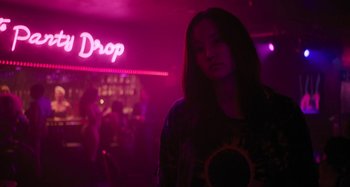 Movie still from “Mona Lisa and the Blood Moon” (2021), directed by Ana Lily Amirpour – A woman standing in front of a neon sign in a dark room; Medium shot, Low angle