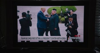 Movie still from “Mona Lisa and the Blood Moon” (2021), directed by Ana Lily Amirpour – A television screen showing a news story with a picture of president donald trump and kim jong un shaking hands; Extreme Wide shot, Over the shoulder angle