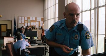 Movie still from “Mona Lisa and the Blood Moon” (2021), directed by Ana Lily Amirpour – A police officer is holding a donut in his hand; Medium shot, Over the shoulder angle