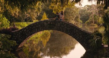 Movie still from “Mona Lisa and the Blood Moon” (2021), directed by Ana Lily Amirpour – Two people are sitting on a bridge over a river; Extreme Wide shot, High angle