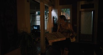 Movie still from “Mona Lisa and the Blood Moon” (2021), directed by Ana Lily Amirpour – A woman carrying a box of pizza in a room; Wide shot, Low angle