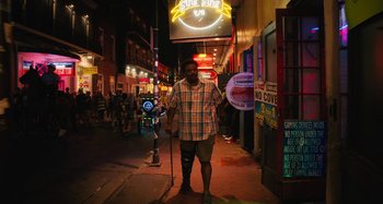 Movie still from “Mona Lisa and the Blood Moon” (2021), directed by Ana Lily Amirpour – A man in a plaid shirt standing on the sidewalk; Wide shot, Low angle