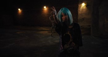 Movie still from “Mona Lisa and the Blood Moon” (2021), directed by Ana Lily Amirpour – A person with blue hair holding a pair of handcuffs; Medium shot, High angle