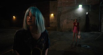 Movie still from “Mona Lisa and the Blood Moon” (2021), directed by Ana Lily Amirpour – A woman with blue hair standing next to another woman in a dark room; Medium shot, Over the shoulder angle