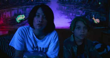 Movie still from “Mona Lisa and the Blood Moon” (2021), directed by Ana Lily Amirpour – Two young people sitting in a dark room; Medium shot, Low angle