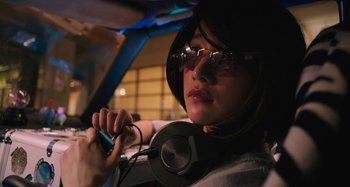 Movie still from “Mona Lisa and the Blood Moon” (2021), directed by Ana Lily Amirpour – A person with headphones and a cell phone in a car; Close Up shot, Low angle