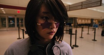 Movie still from “Mona Lisa and the Blood Moon” (2021), directed by Ana Lily Amirpour – A woman wearing glasses and a star shaped sticker on her face; Close Up shot, Over the shoulder angle