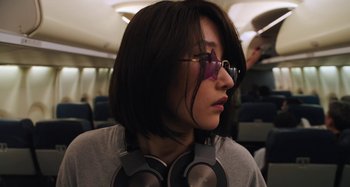 Movie still from “Mona Lisa and the Blood Moon” (2021), directed by Ana Lily Amirpour – A person with glasses and headphones on a plane; Close Up shot, Low angle