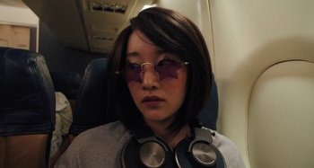 Movie still from “Mona Lisa and the Blood Moon” (2021), directed by Ana Lily Amirpour – A woman with glasses and headphones on a plane; Close Up shot, High angle