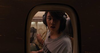 Movie still from “Mona Lisa and the Blood Moon” (2021), directed by Ana Lily Amirpour – A person wearing headphones on an airplane looking out a window; Medium shot, Over the shoulder angle