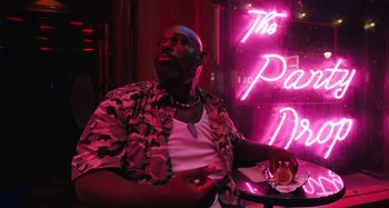 Movie still from “Mona Lisa and the Blood Moon” (2021), directed by Ana Lily Amirpour – A man sitting at a table in front of a neon sign; Medium shot, Low angle